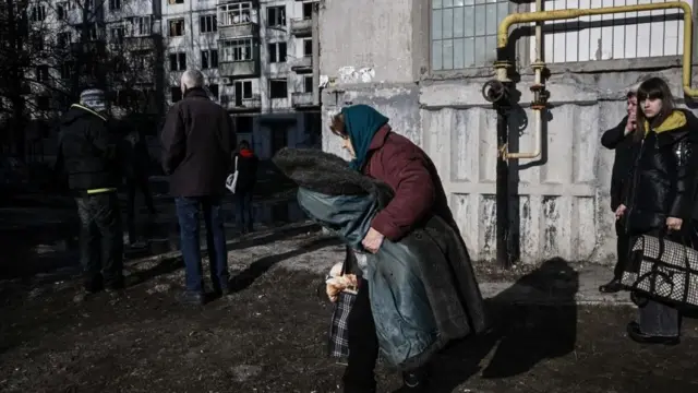 கிழக்கு உக்ரைன் நகரமான சுகுவே மீது நடந்த குண்டுவெடிப்புகளுக்குப் பிறகு, ஓர் இடிந்த கட்டிடத்தில் இருந்து மக்கள் வெளியேறினர்