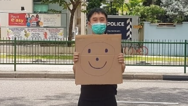 范国瀚在新加坡大巴窑邻里警局外举起画上笑脸的纸皮（范国瀚提供照片28/3/2020）