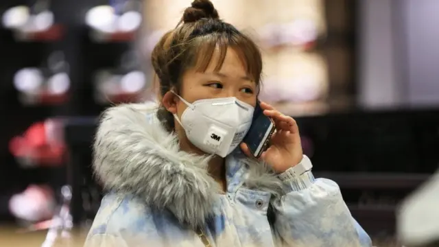A woman wearing a protective mask uses a smartphone as she shops at a shopping mall in Shenyang in China