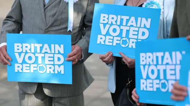 Troje ljudi drži u rukama parole za partiju Reform UK plave boje