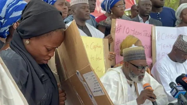 Des femmes et des hommes se rassemblent pour commémorer les dix ans de l'enlèvement de 276 jeunes filles à Chibok, dont beaucoup sont toujours portées disparues. Une femme en détresse, le visage voilé de noir, brandit une pancarte, tandis qu'un homme, micro en main, s'adresse à la foule.