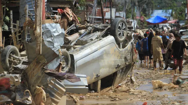 Sejumlah warga melintas di dekat mobil warga yang terbawa arus banjir di kawasan Desa Bukit Tempurung, Kota Kuala Simpang, Kabupaten Aceh Tamiang, Aceh, Rabu (3/12/2025).