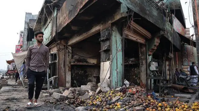 A man walks besides a burnt fruit shop after a parking space was set on fire by a mob during riots in Chandbagh area of New Delhi, India on 29 February 2020.