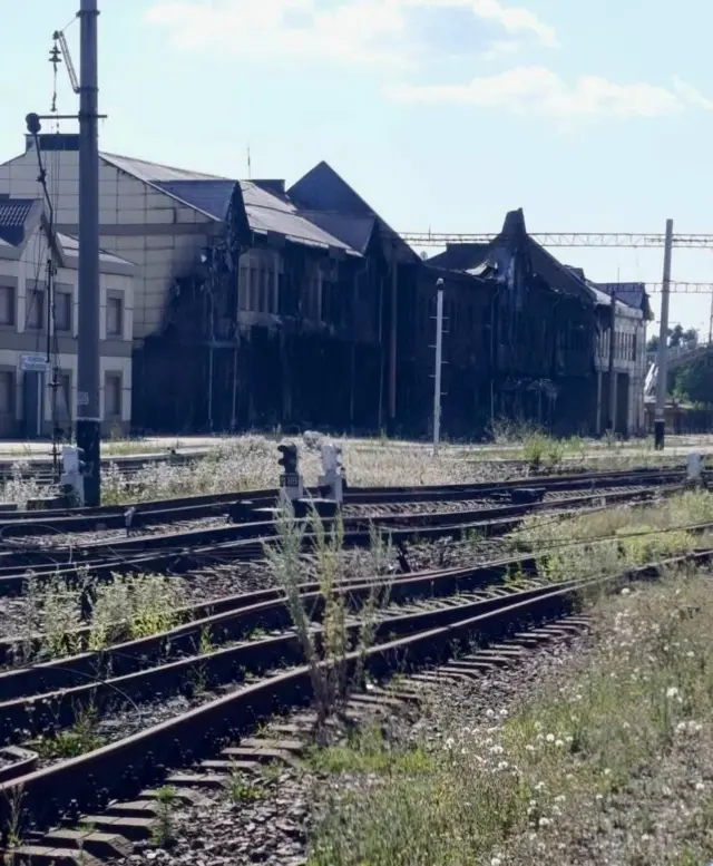 Колії у траві на фоні обгорілої будівлі вокзалу 