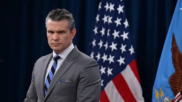 Pete Hegseth üstünde bir takım elbiseyle, arkasında Amerikan bayrağıyla kürsüde