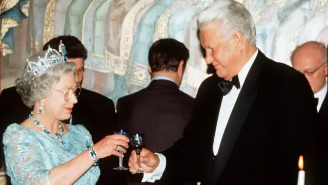 A rainha Elizabeth 2ª, vestindo um vestido azul claro e uma tiara, brinda a Boris Yeltsin (à direita), que está de smoking.