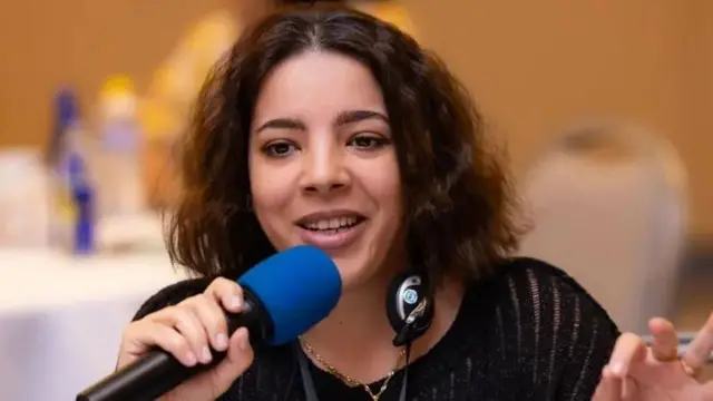 آلا محمد میکروفون به دست در حال سخنرانی