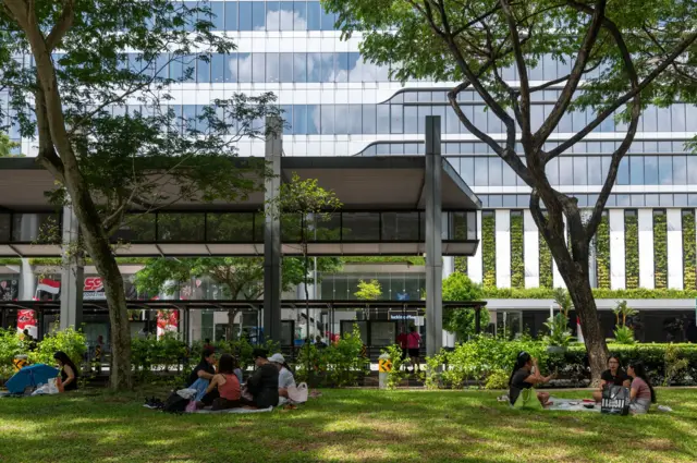 Warga menikmati piknik di Dhoby Ghaut Green, yang terletak di Orchard Road di Singapura, duduk di atas rumput di bawah pepohonan.