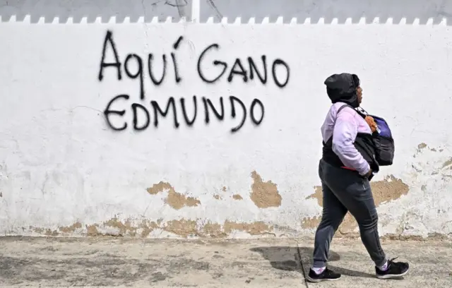 Una mujer camina por una calle donde hay un grafiti que dice "aquí ganó Edmundo".