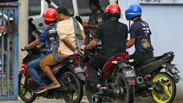 မလေးရှားရဲ့ လူဝင်မှုကြီးကြပ်ရေးရဲတွေ ထိန်းသိမ်းရေးစခန်းထဲက ထွက်ပြေးတဲ့ ရိုဟင်ဂျာတစ်ဦးကို လက်ထိပ်ခတ် ပြီး စခန်းဆီခေါ်ဆောင်လာတဲ့မြင်ကွင်း (ပုံဟောင်း)