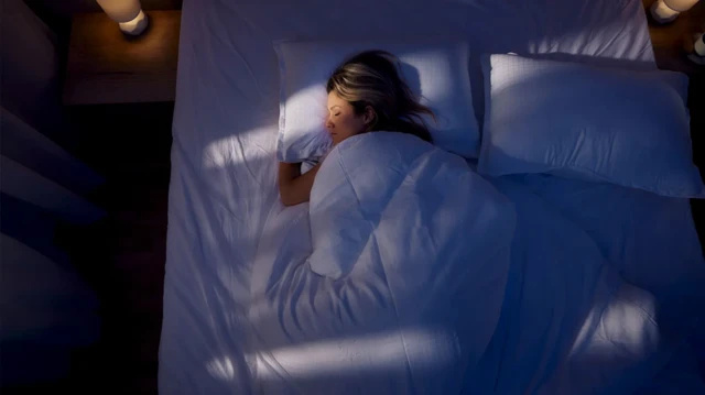 Une femme dormant sous sa couette avec une lumière diffuse de lampes veilleuses.
