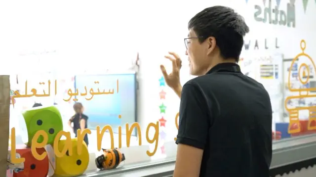 صورة تُظهر والداً يقف خلف زجاج استديو التعليم في إحدى المدارس الخاصة في الإمارات وهو ينظر إلى ابنه داخل الصف ويضع يده على الزجاج.