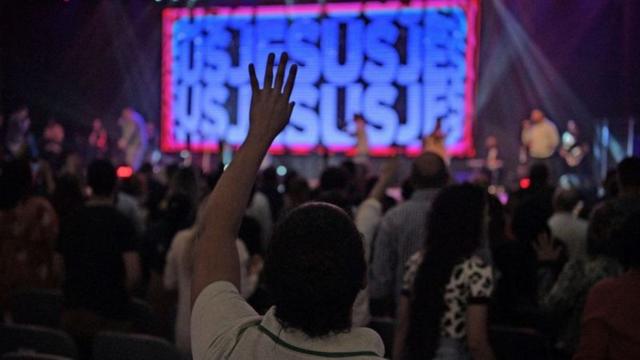 Mão erguida em multidão com neon escrito Jesus ao fundo