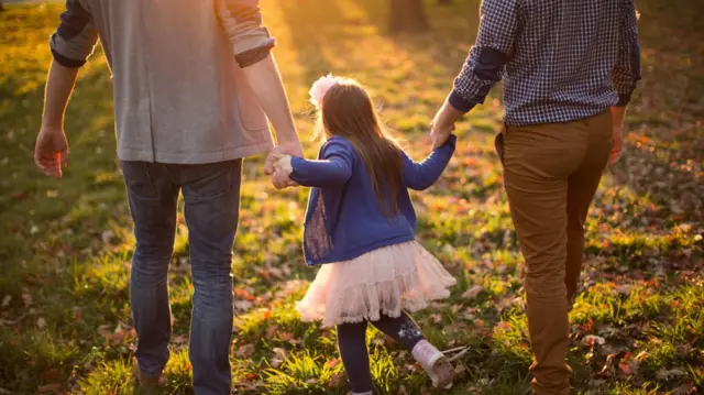 A child walking with a gay couple and holding hands