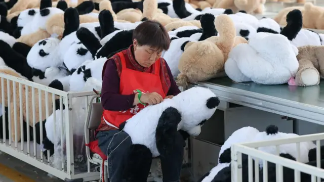 Bir fabrikada bir kadın sevimli oyuncak pandalar dikiyor