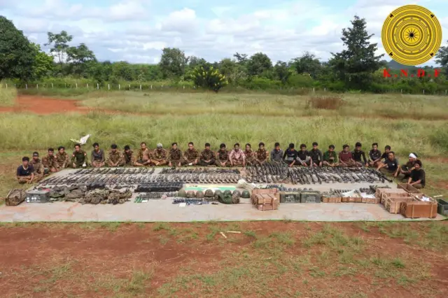 ကွင်းပြင်ထဲမှာ သိမ်းဆည်းရမိတဲ့ စစ်လက်နက်အမျိုးအစားအစုံကို ခင်းကျင်းပြသထားပြီး ဖမ်းဆီးခံထားရတဲ့ မြန်မာစစ်တပ်က စစ်ဝတ်စုံရော အရပ်ဝတ်ပါ ဝတ်ဆင်ထားတဲ့ စစ်သုံ့ပန်းတွေက ဝန်းရံထိုင်နေကြပါတယ် 