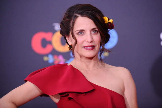 Alanna Ubach con un vestido rojo, con un hombro descubierto. Detrás tiene una pared que dice "Coco"