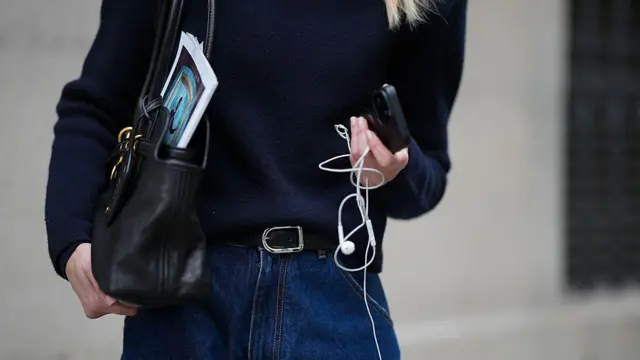 Mulher segurando fones de ouvido com fio e um celular. 