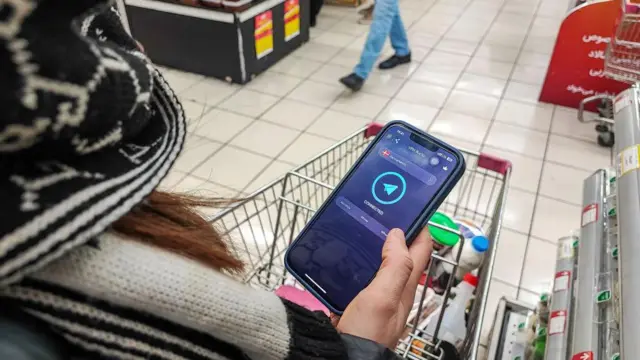 یک شهروند ایرانی پس از فعالکردن یک شبکه خصوصی مجازی (وی پی ان) برای دسترسی به اینترنت، در حالی که در یک سوپرمارکت در تهران مشغول خرید است، تلفن همراه خود را در دست دارد.