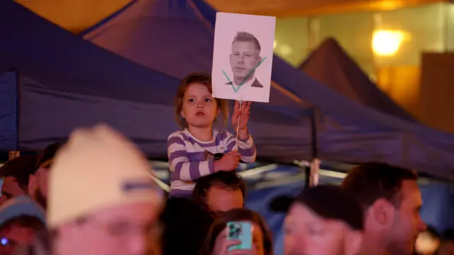 طفلة محمولة على الأكتاف تحمل صورة بيتر ماغيار وسط الحشود.