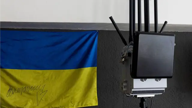 На стене висит флаг Украины, рядом закреплено небольшое электронное устройство с несколькими антеннами и проводами.