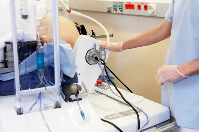 Людина в медичному одязі та рукавичках тримається за прилад у кабінеті