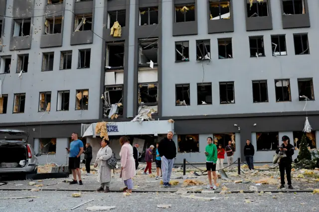 Mieszkańcy stoją przed bydynkiem, który został trafiony rosyjskimi rakietami i dronami podczas ataku Rosji na Ukrainę