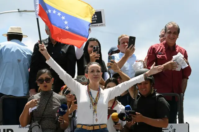 María Corina Machado erguendo os braços em palco