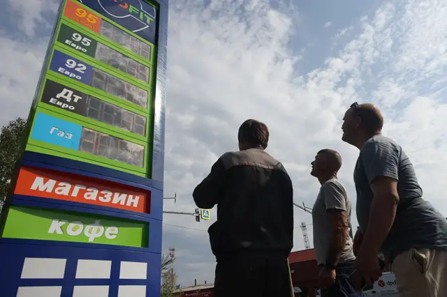Люди дивляться на табло з цінами на пальне на автозаправній станції.