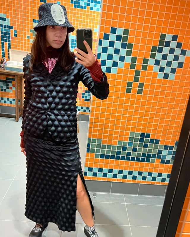 Monica Salley porte un ensemble noir avec des bosses noires (qui ressemblent à des ventouses)