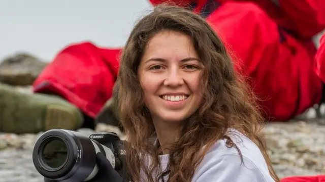 Danielle Waldman sorrindo para a câmera e segurando uma máquina fotográfica