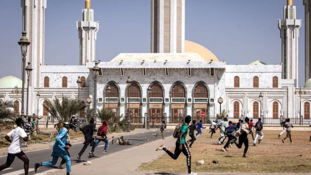 Des manifestants passent devant une mosquée à Dakar alors que les forces de sécurité tirent des gaz lacrymogènes