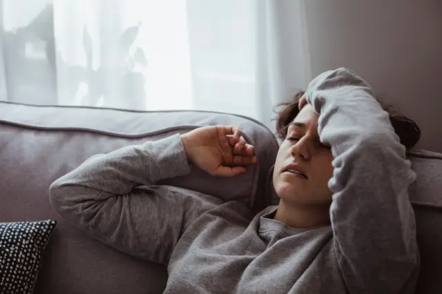 Koltukta yatan başını tutmuş bir kadın