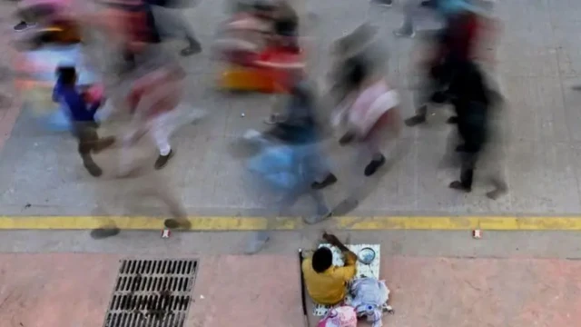 ਸੜਕ ਤੋਂ ਲੰਘਦੇ ਲੋਕ ਤੇ ਇੱਕ ਪਾਸੇ ਬੈਠਾ ਮੰਗਤਾ