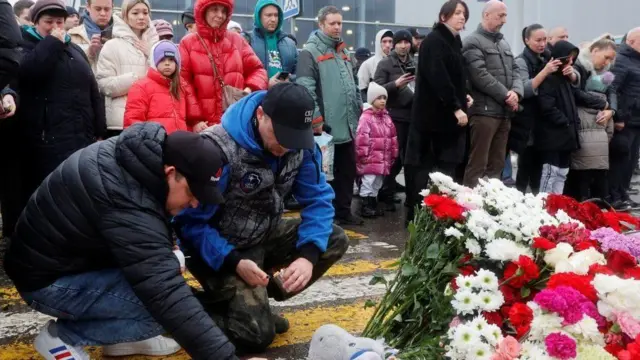 Men light candles for makeshift memorial for di Crocus City Hall