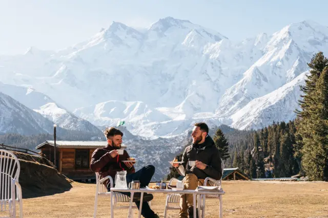 Two men having breakfast with Nanga Parbat mountain view in the backdrop