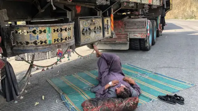 یک راننده لاری که در مرز میان افغانستان و پاکستان زیر سایه موترش دراز کشیده است