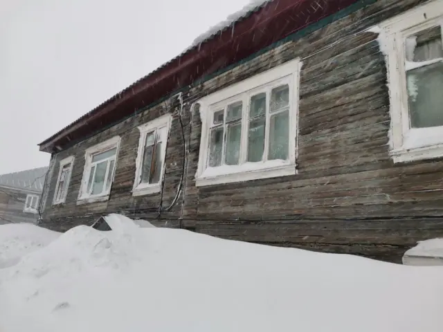 На фото старый деревянный двухэтажный дом, первый этаж полностью скрыт под снегом