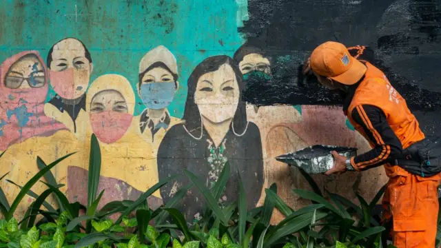 Seorang petugas menghapus mural yang memperingati masyarakat untuk terus memakai masker pada Selasa (9/5)