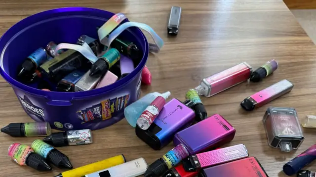 Varios vaporizadores estaban esparcidos sobre el escritorio del director. Algunos estaban guardados en una caja de bombones Heroes.