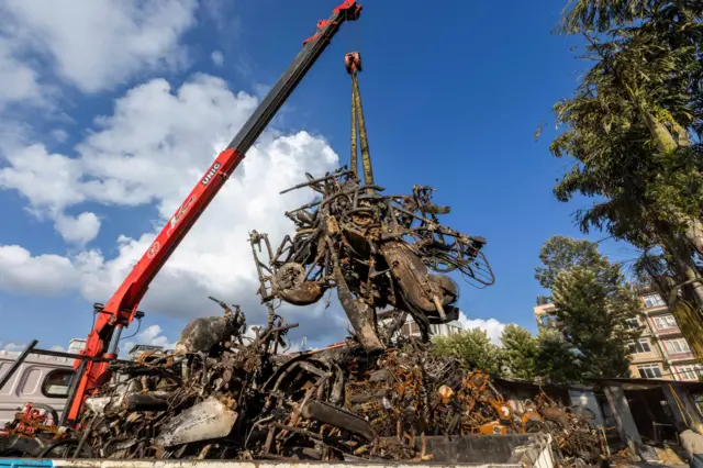 क्रेनको मद्दतले जलेका मोटरसाइकलको भग्नावशेषलाई संसद् भवन परिसरमा जम्मा गरिँदै।