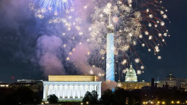 ライトアップされた連邦議会議事堂のドーム屋根、ろうそくの映像が投影されたワシントン記念塔、ライトアップされたリンカーン記念堂の上に金色の花火が打ち上げられている