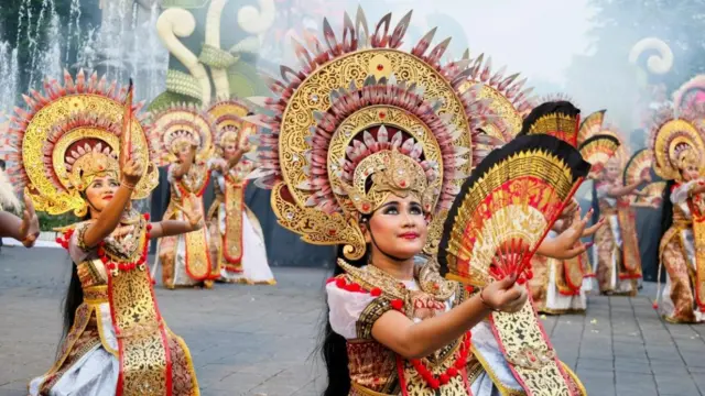 金色の頭飾りをつけ、扇子のようなものを右手に持った女性ダンサーが、路上に膝をついて踊っている