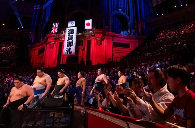 ロイヤル・アルバート・ホールの壮麗な壁が赤く照らされ、日英の国旗と共に「満員御礼」と書かれた垂れ幕が下げられている