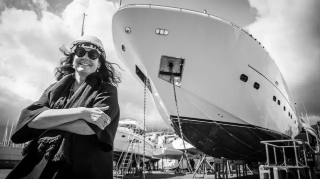 Barbara Amerio sorri para a câmara em frente. Atrás dela há vários superiates