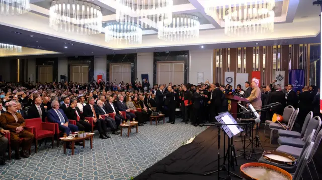 Barzani, 4. Uluslararası Melayê Cizîrî Sempozyumu'nda konuşma yapıyor. Katılımcılar izliyor.