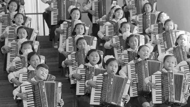 کودکان کره شمالی در چهار ردیف نشسته روی پلکانها در حالی که هر یک مشغول نواختن آکاردئون است