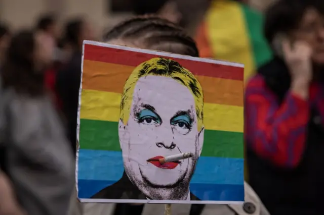 Демонстрант держит транспарант с изображением премьер-министра Венгрии Виктора Орбана на фоне флага ЛГБТК+ во время протеста против закона, направленного на запрет мероприятий ЛГБТК+-прайда, 25 марта 2025 года в Будапеште, Венгрия. 