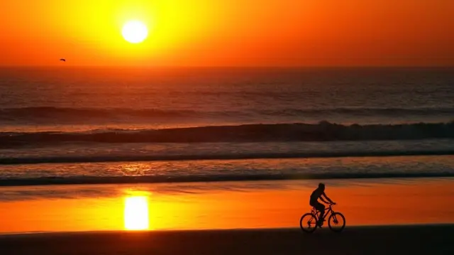 Pessoa andandocomo ganhar na roleta do cassinobicicleta à beira do mar ao pôr do sol 