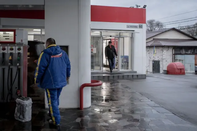 Заправна станція, чоловік стоїть біля пістолета з бензином, біля нього каністра